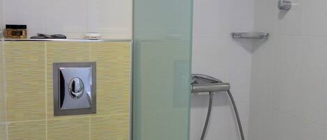 Un baño con inodoro, ducha con mampara de vidrio y una toalla sobre el asiento.