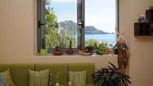 A room with a large window overlooking a coastal landscape, a green sofa, and various potted plants. - Horizon Beach Hotel (Agios Vasileios)