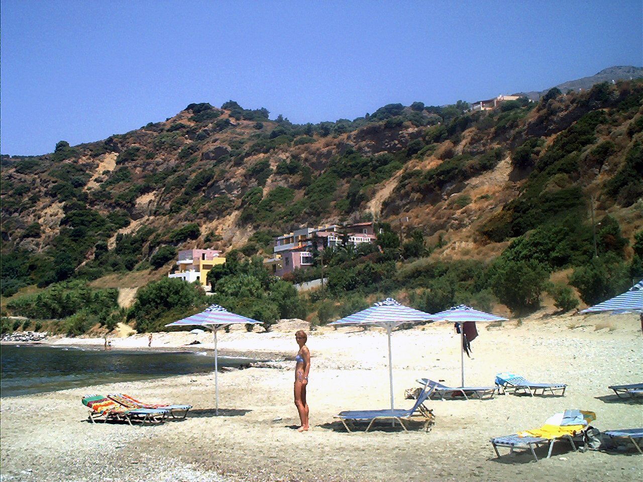 A beach with umbrellas, lounge chairs, and a person standing.