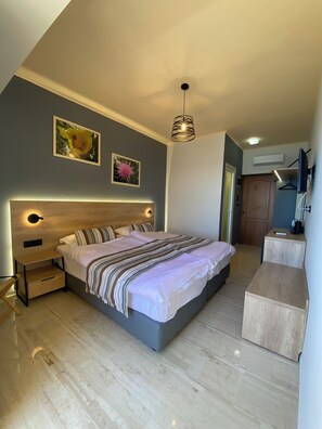 Un dormitorio moderno con una cama grande, mesitas de noche, una lámpara colgante y dos cuadros en la pared.