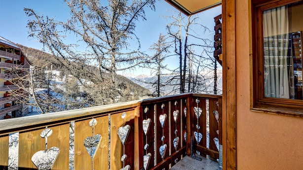 A wooden balcony with heart-shaped cutouts, overlooking a snowy landscape with mountains in the background. - Vacancéole - Résidence Vega (Risoul)