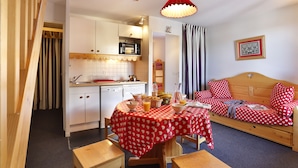 A cozy room with a kitchenette, a dining table with a red tablecloth, and a bed with red and white polka dot bedding. - Vacancéole - Résidence Vega (Risoul)