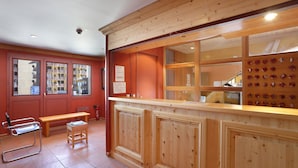 A reception area with a wooden counter, a bench, and a small table. - Vacancéole - Résidence Vega (Risoul)