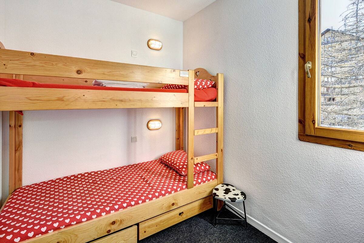 Una cama litera con colcha de lunares rojos, una escalera de madera y un taburete con cojín estampado con vacas.