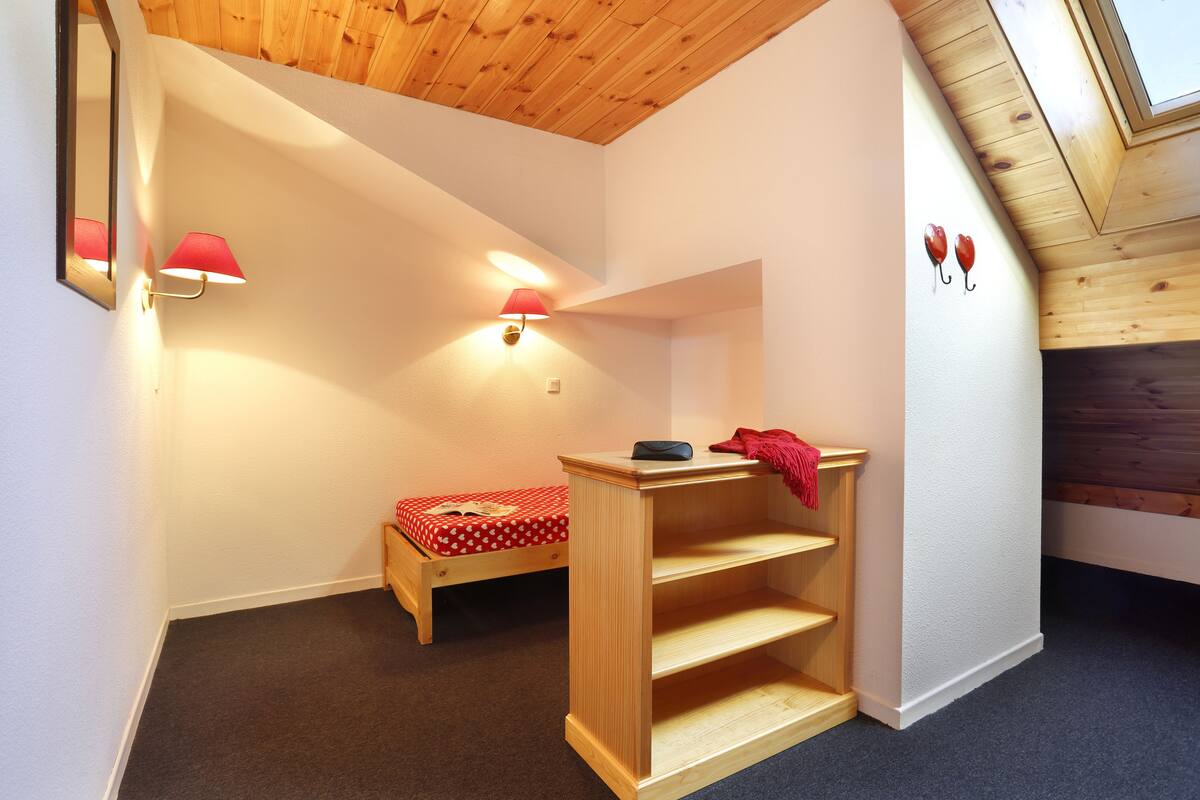 Una habitación pequeña y acogedora con una cama de madera, una mesita de noche y un estante empotrado.