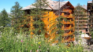 A wooden cabin with a sloped roof surrounded by lush greenery and trees. - Vacancéole - Résidence Vega (Risoul)