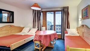 A room with two wooden beds, a small table with a red heart-patterned tablecloth, and a window with curtains. - Vacancéole - Résidence Vega (Risoul)