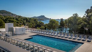 A pool with lounge chairs, a clear view of the sea, and a mountainous backdrop. - SOWELL RÉSIDENCES Les Chênes Verts (Saint-Raphael)