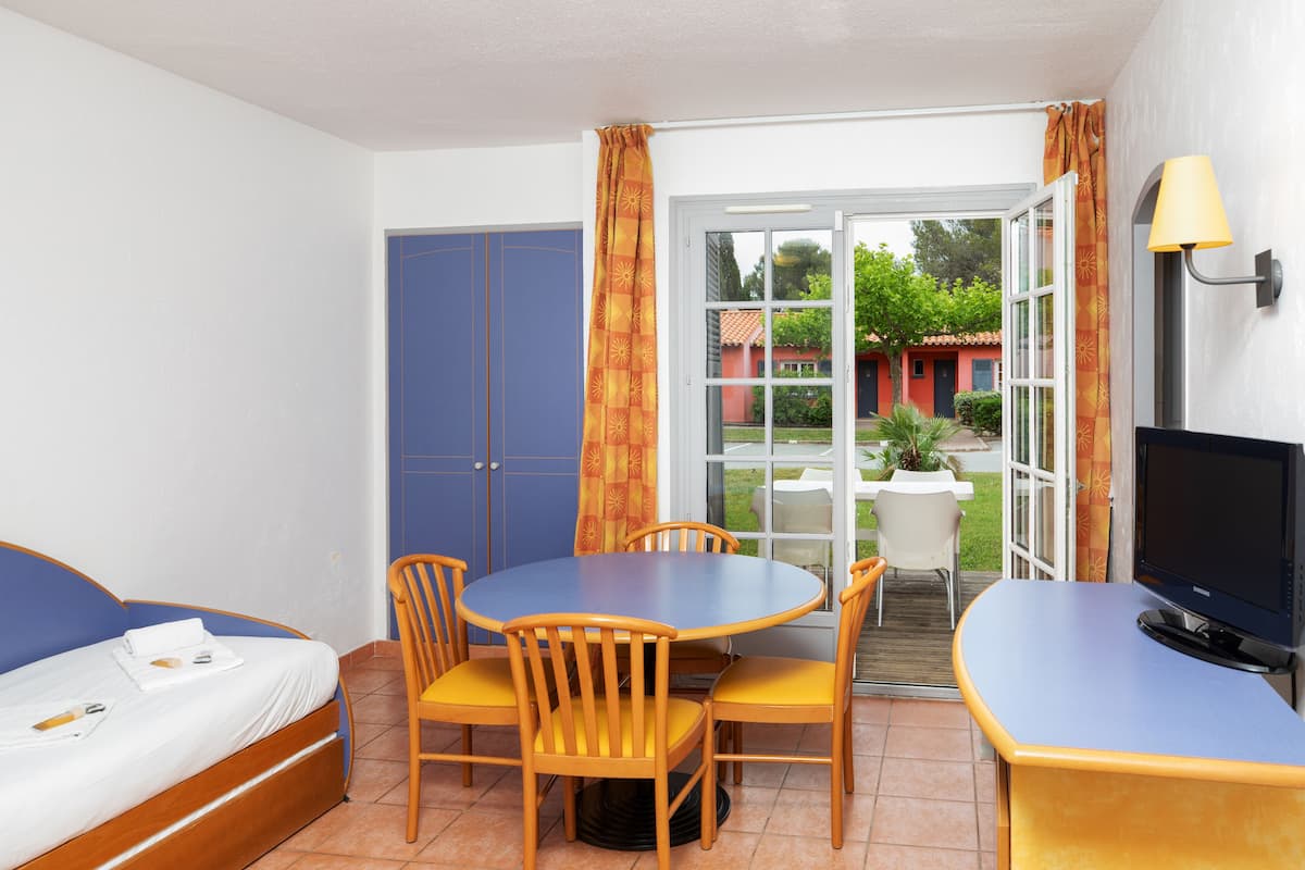 Una habitación con cama, una mesa de comedor con sillas, un televisor y un ventanal corredero que da a un espacio exterior.