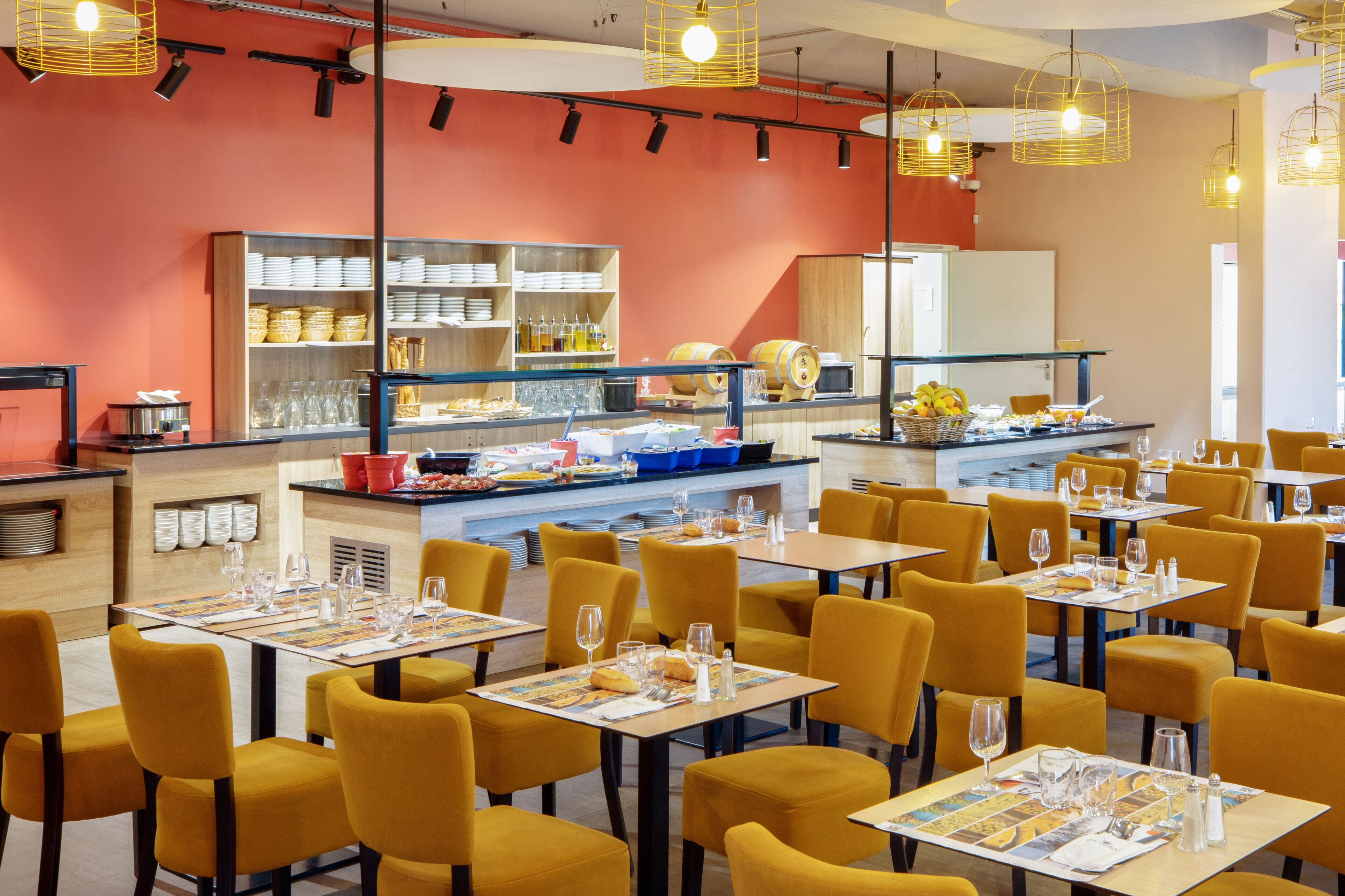 Una sala ristorante con sedie e tavoli gialli, un'area buffet con cibo e bevande, e un bancone con una cassa.