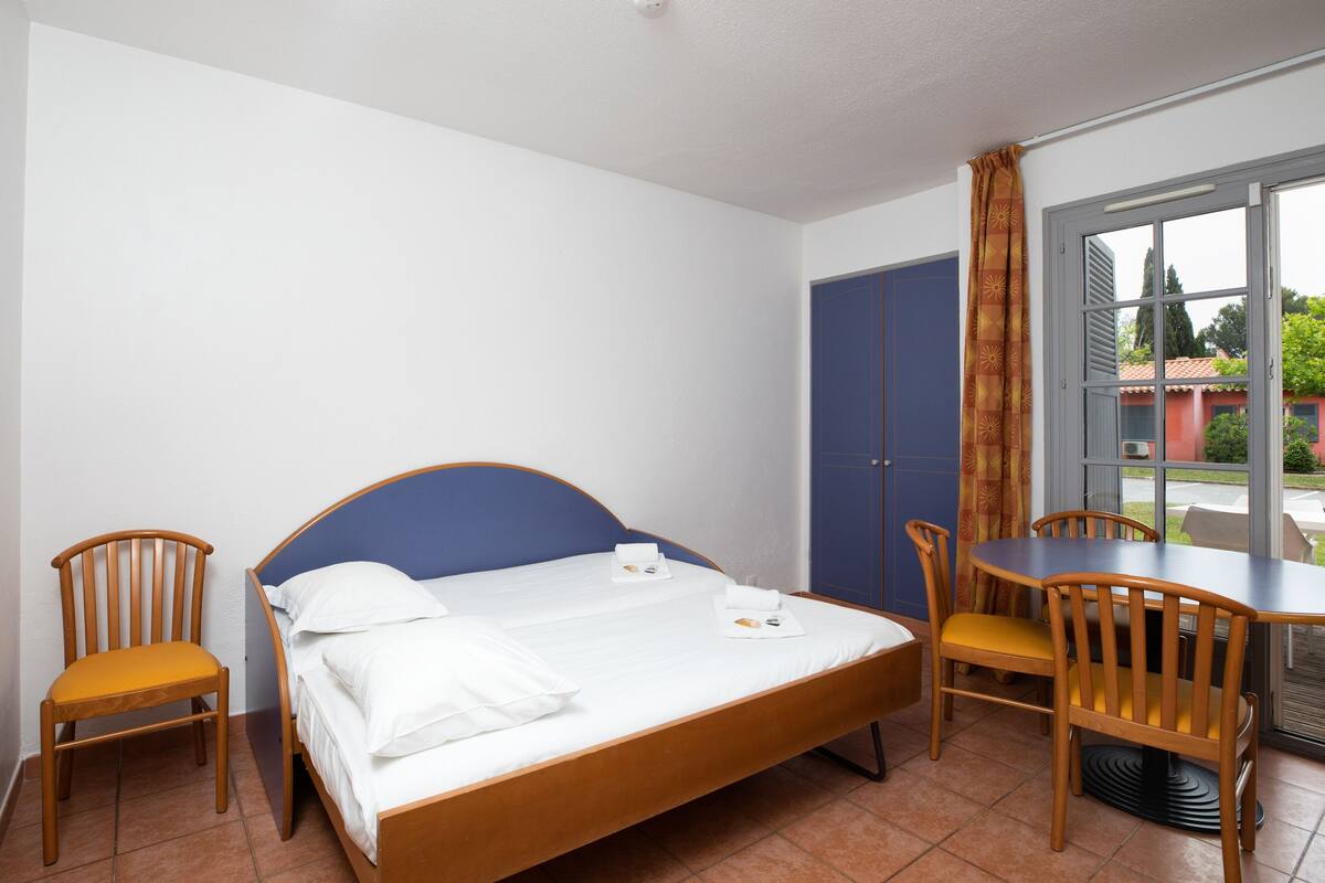 Habitación de hotel con cama, dos sillas de madera, una mesita y una ventana con cortinas.
