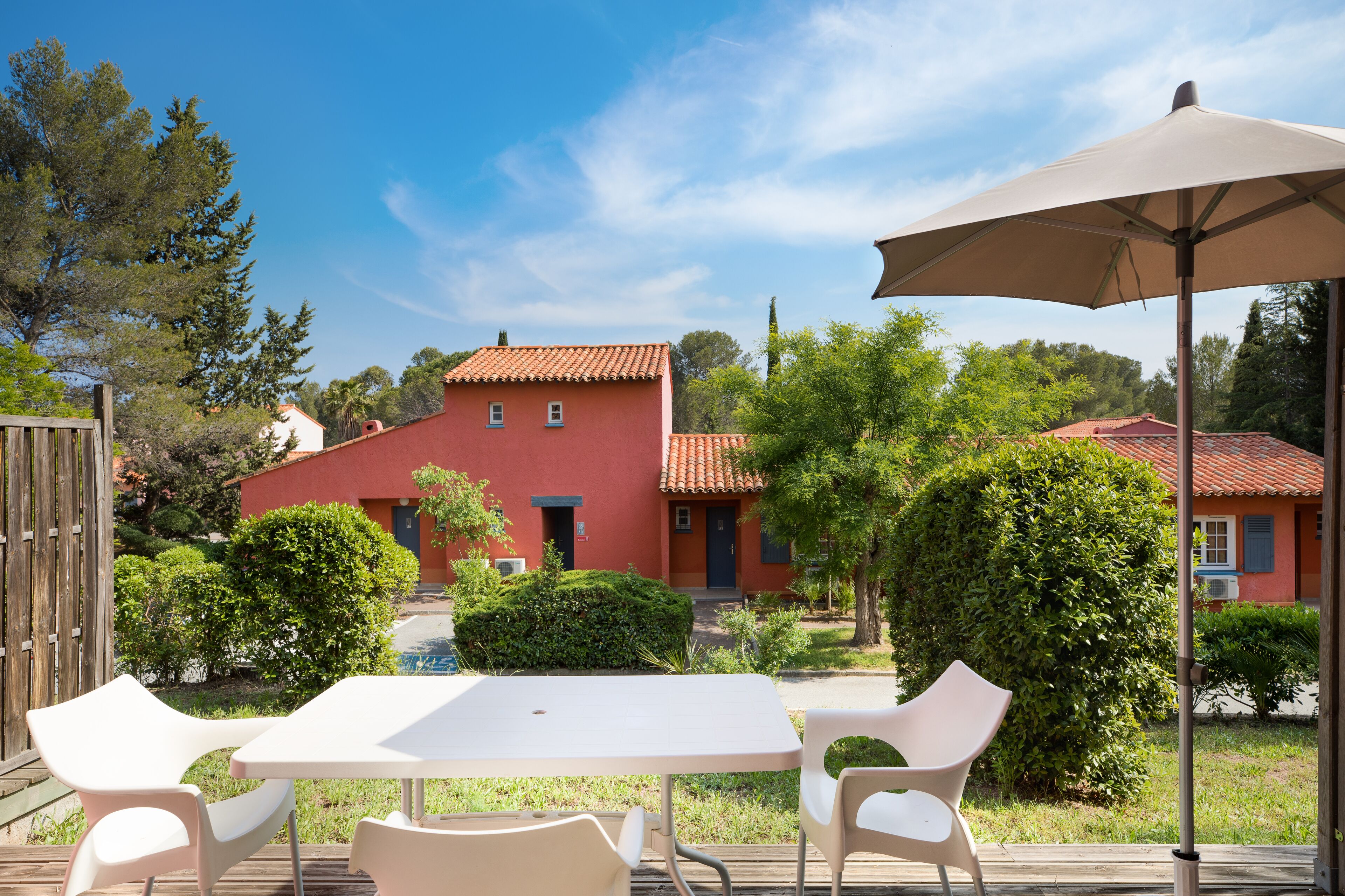 Un patio al aire libre con mesa y sillas, una pérgola con toldo y un edificio rojo al fondo.