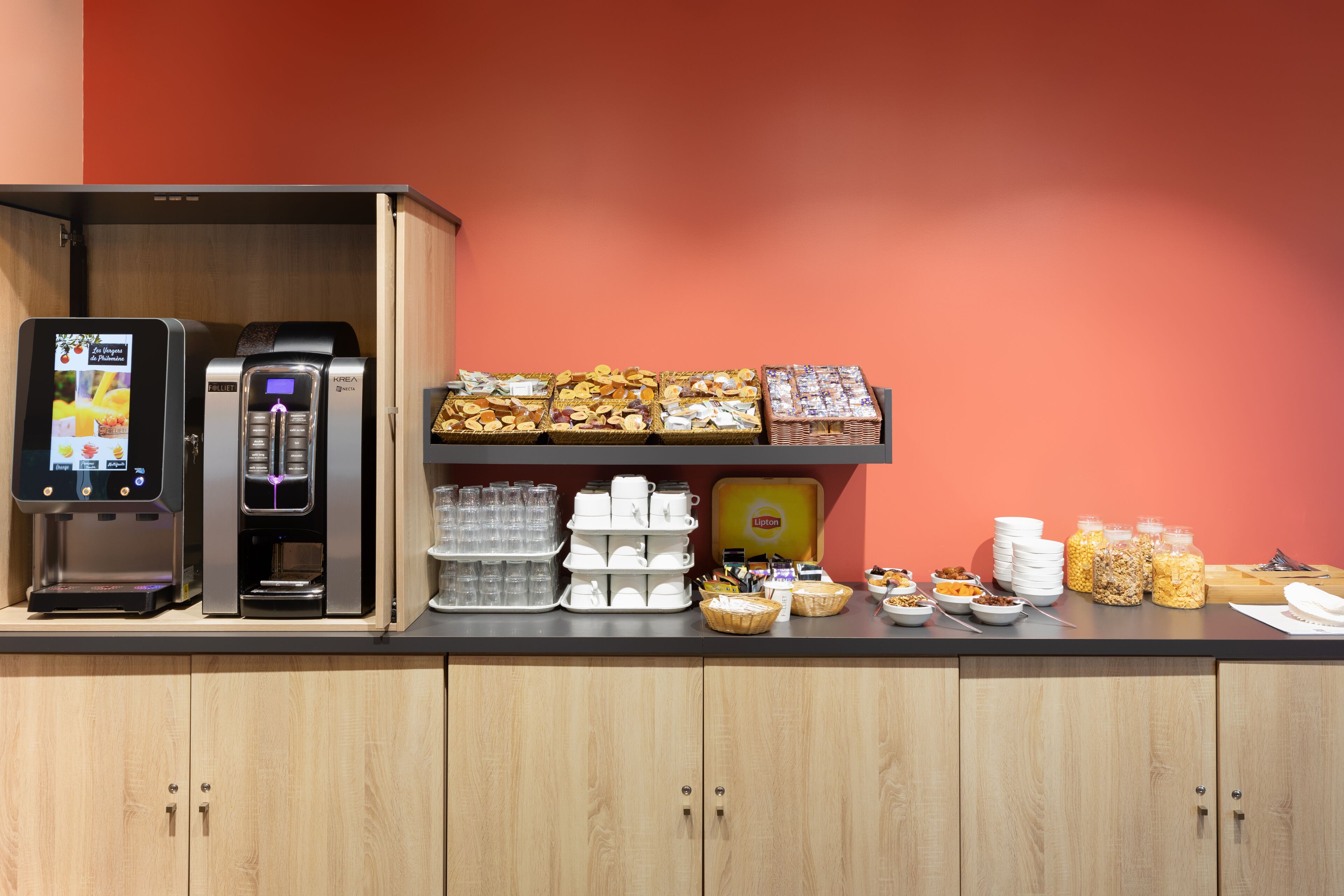 Un buffet pour le petit-déjeuner, où chacun se sert, avec des machines à café, un assortiment de viennoiseries et divers produits pour le petit-déjeuner.