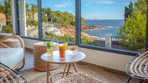 A balcony with wicker furniture, a small round table with drinks, and a view of the sea and rocky coastline. - SOWELL RÉSIDENCES Les Chênes Verts (Saint-Raphael)