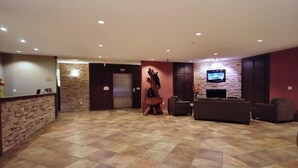 A lobby with a reception desk, a stone wall, a fireplace, and a television mounted on the wall. - Sigma Inn & Suites Hudson's Hope (Hudson's Hope)