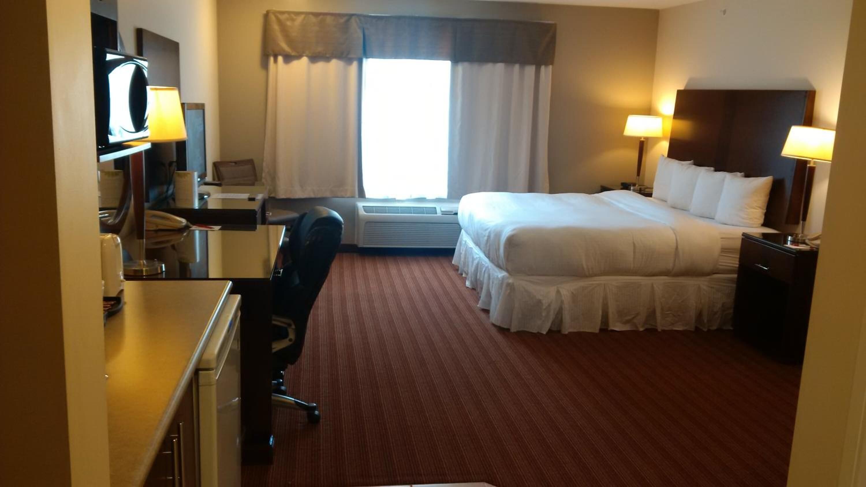 Quarto de hotel com cama, escrivaninha, cadeira e televisão.