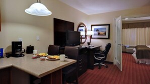 A hotel room with a dining area, a desk with a computer, a television, a bed, and a bathroom. - Sigma Inn & Suites Hudson's Hope (Hudson's Hope)