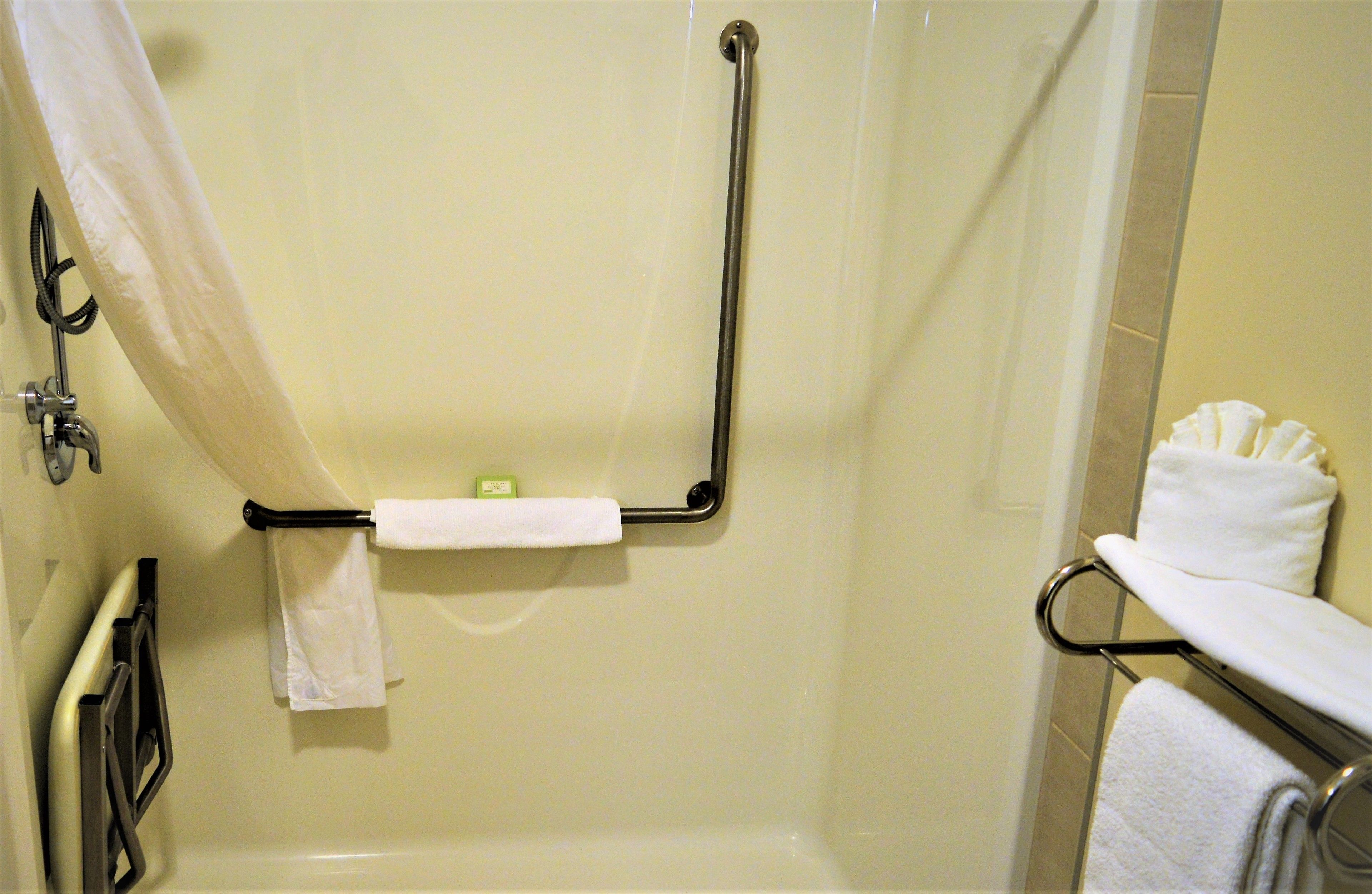 A bathroom with a shower, grab bars, and a towel rack.