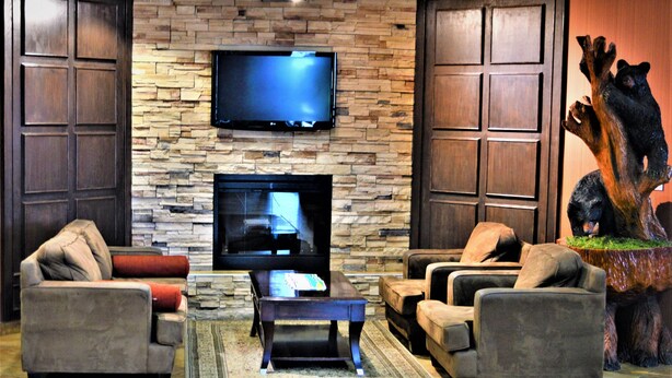 A living room with a stone fireplace, a flat-screen TV, and a bear statue. - Sigma Inn & Suites Hudson's Hope (Hudson's Hope)