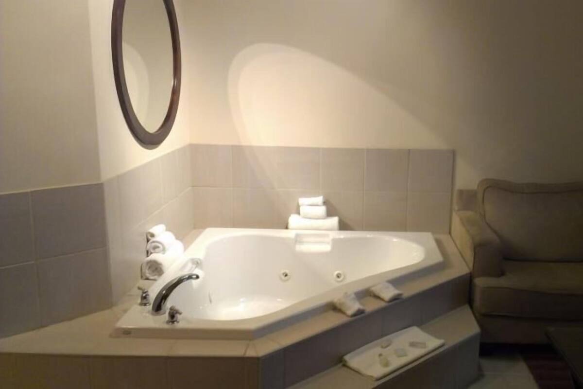 A bathroom with a large bathtub, a mirror, and a beige sofa in the adjacent living area.