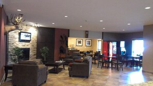 A spacious lobby with a stone fireplace, comfortable seating, a dining area, and a Coca-Cola refrigerator. - Sigma Inn & Suites Hudson's Hope (Hudson's Hope)