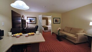 A hotel room with a dining area, a sofa, a TV, and a bed. - Sigma Inn & Suites Hudson's Hope (Hudson's Hope)