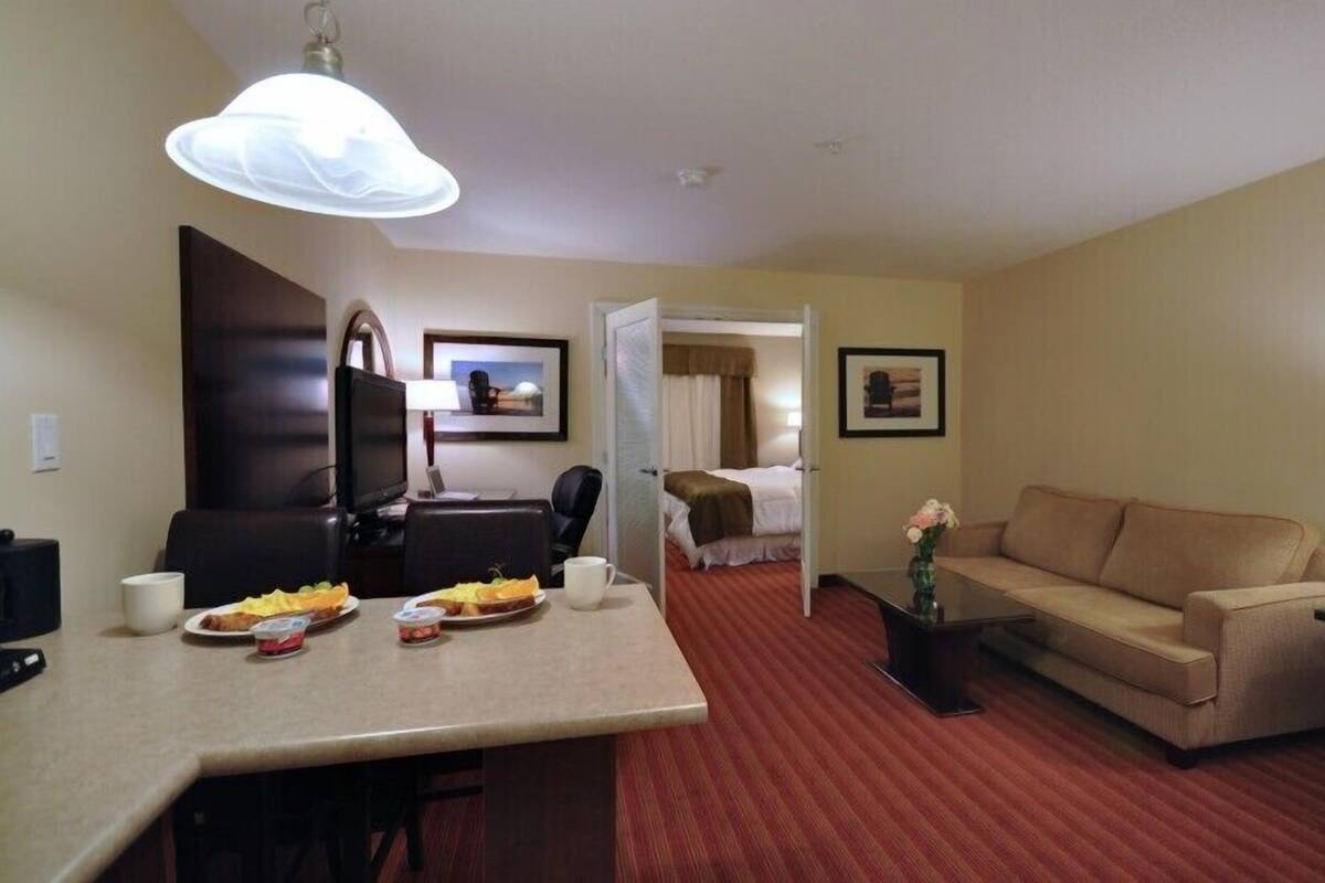 A hotel room with a dining area, a sofa, a TV, and a bed.