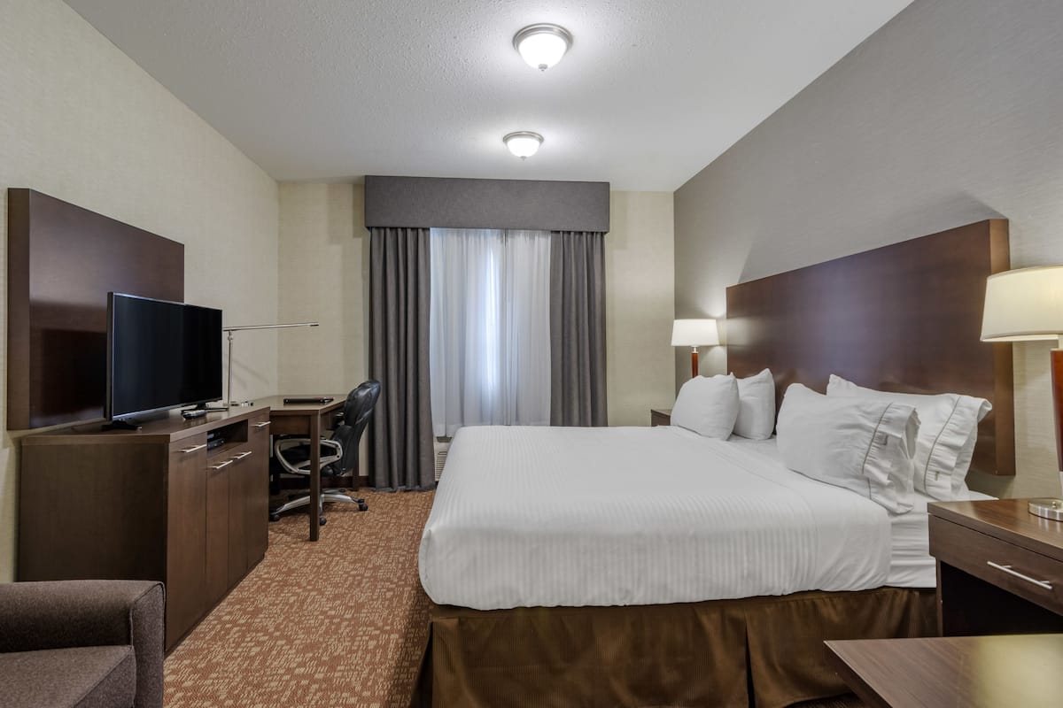 A hotel room with a large bed, a desk with a chair, a TV, and a lamp.