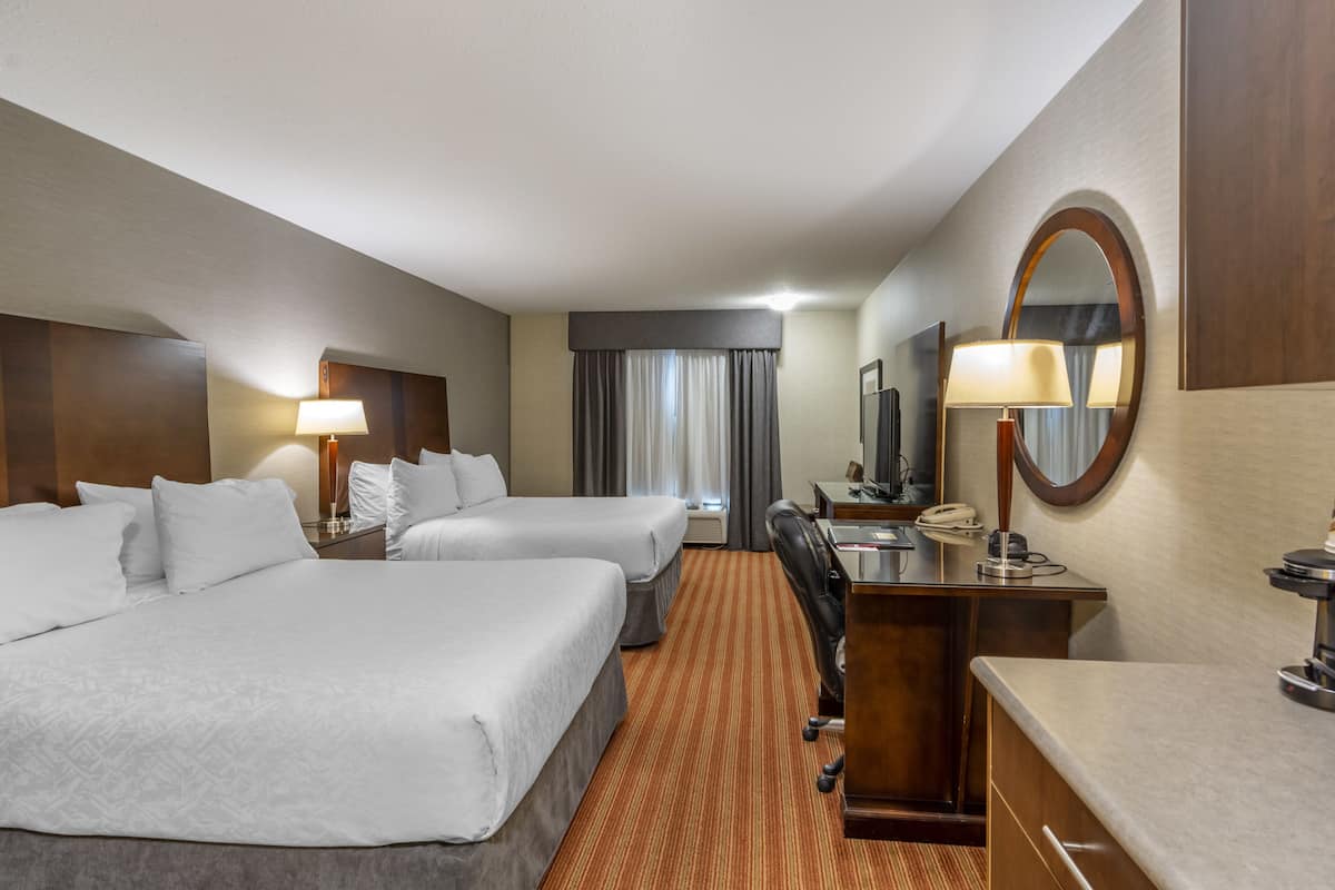 A hotel room with two beds, a desk, a chair, a desk lamp, a telephone, and a mirror.
