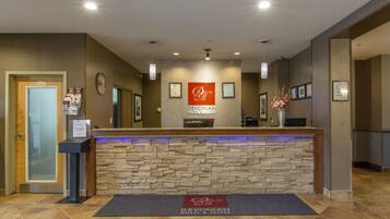A reception desk with a stone facade, a sign reading "Devonian Hotel & Suites", and a blue-lit reception area.