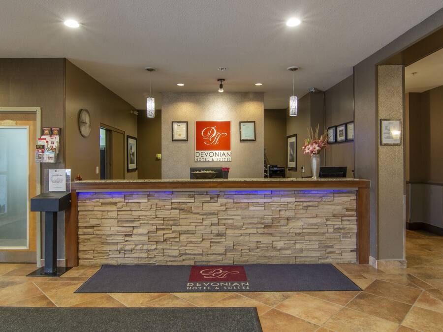 A reception desk with a stone facade, a sign reading "Devonian Hotel & Suites", and a blue-lit reception area.
