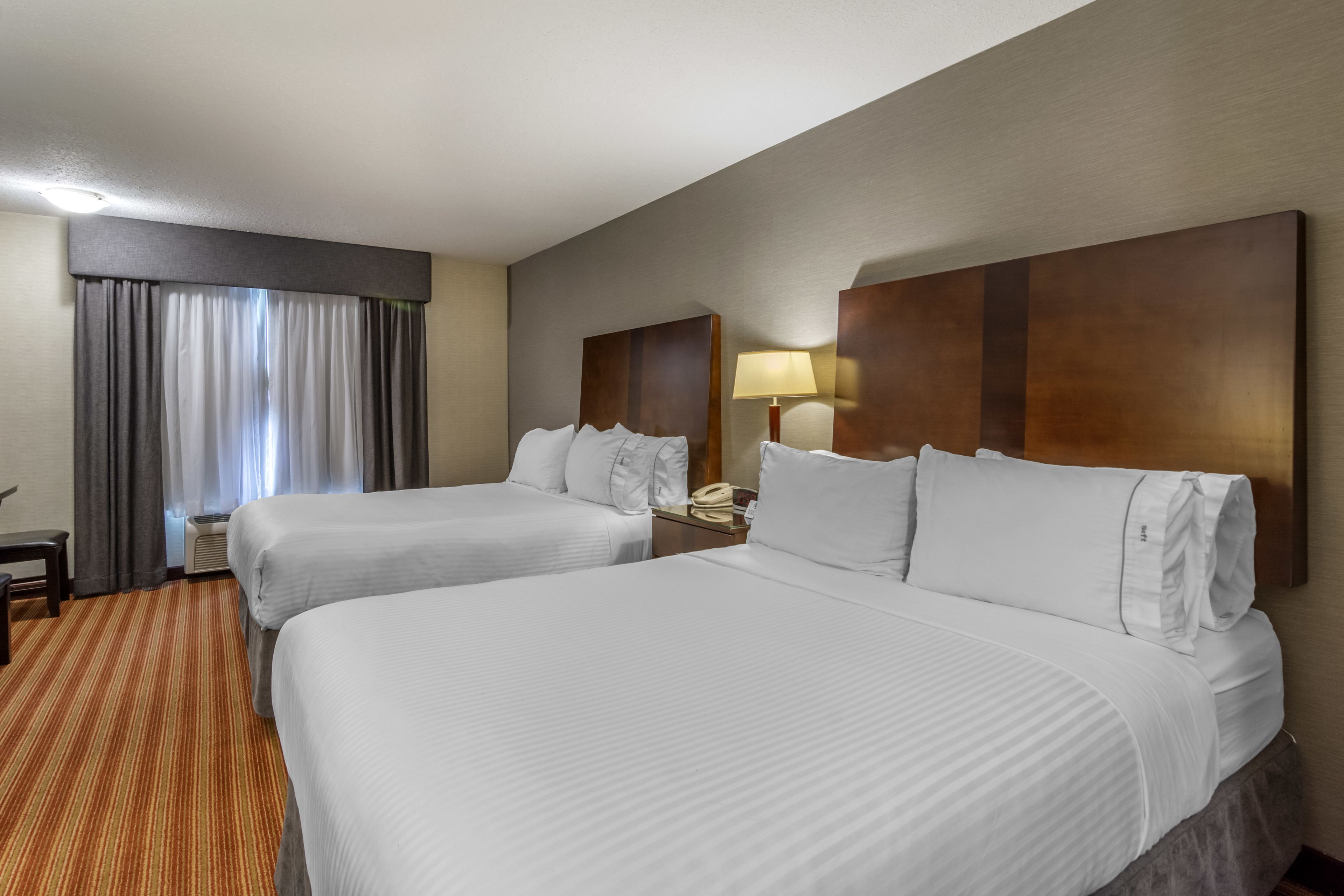 A hotel room with two beds, a desk, a lamp, and a window with curtains.