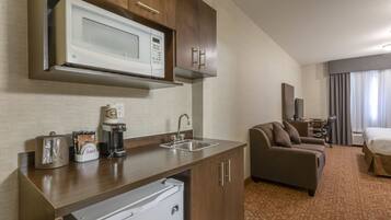 Habitació d'hotel compacta amb cuineta, sofà, llit i televisió.