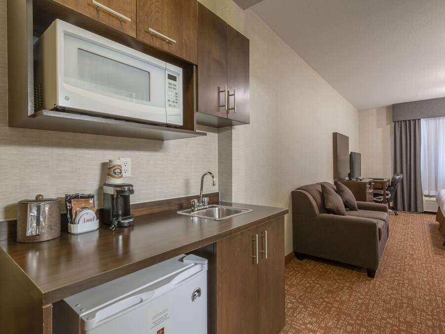 Habitació d'hotel compacta amb cuineta, sofà, llit i televisió.
