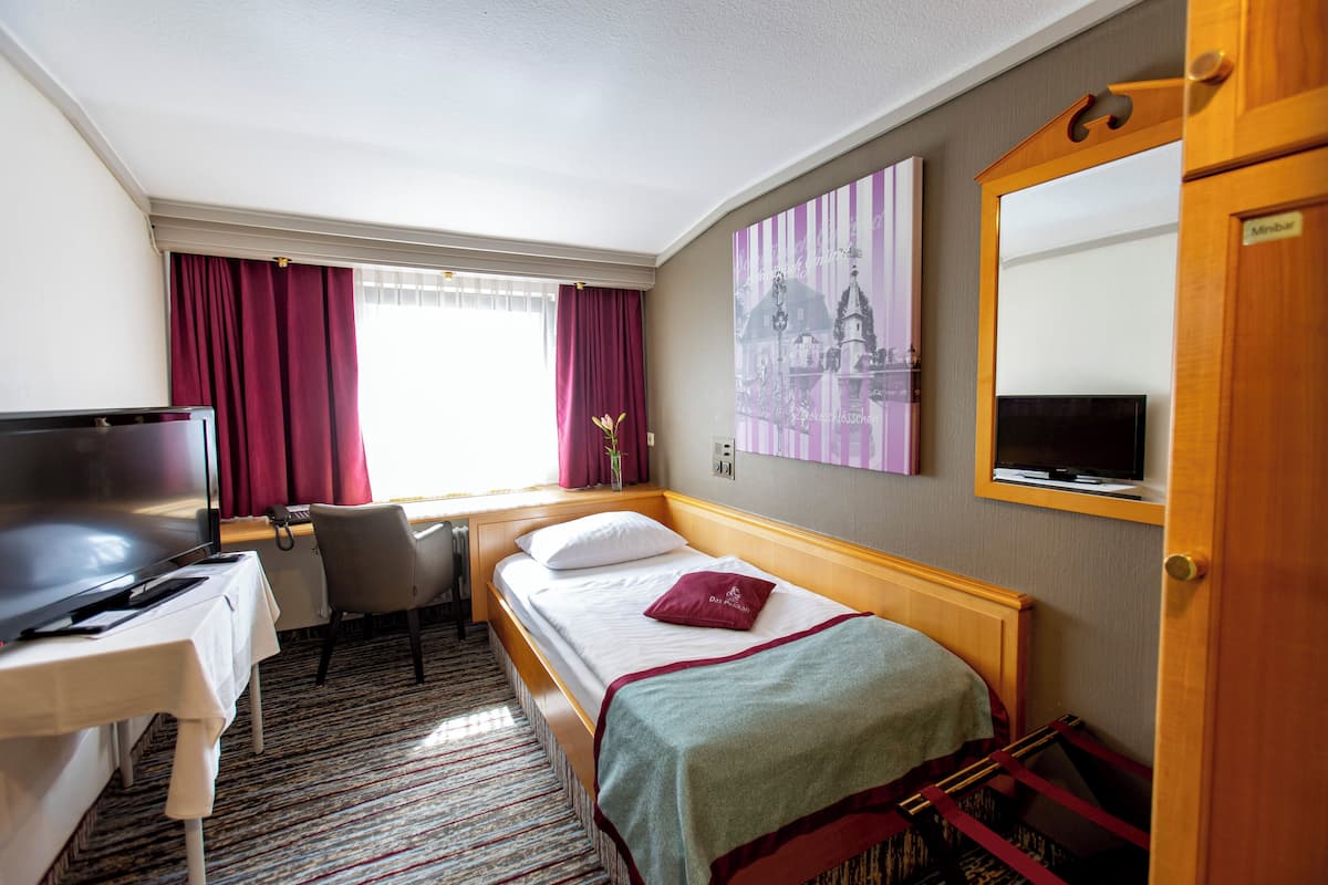Ein Hotelzimmer mit Bett, Schreibtisch mit Fernseher, Stuhl und Fenster mit Vorhängen.