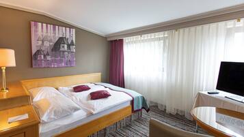 A hotel room with a bed, a desk, a chair, a television, and a painting on the wall.