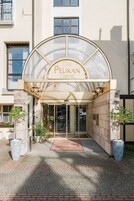 La entrada del Hotel Das Pelikan, con un toldo de cristal y un acceso empedrado con ladrillos.