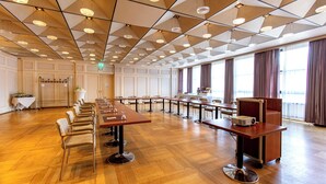 A spacious conference room with long tables and chairs, a projector, and a large window with curtains.