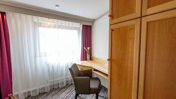 Habitación de hotel con un escritorio de madera, una silla, un ventanal con cortinas traslúcidas y un radiador.