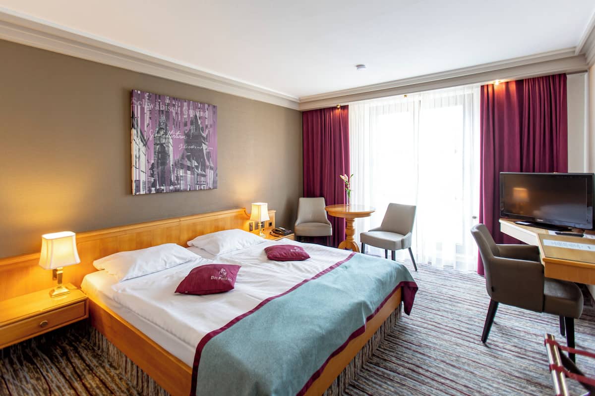 Ein Hotelzimmer mit Bett, Schreibtisch mit Fernseher, Stuhl, Lampe und einem Bild an der Wand.