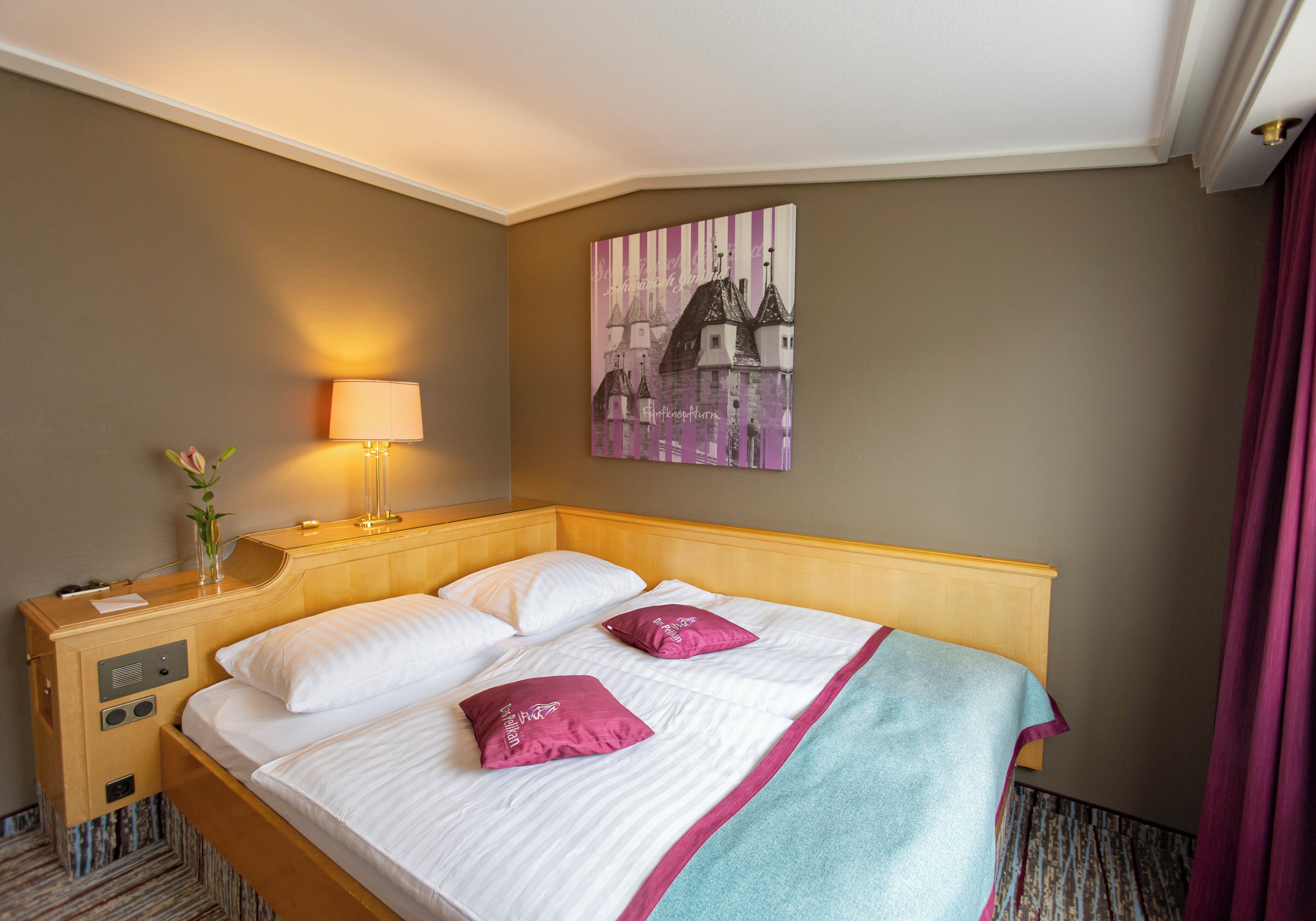 Habitación de hotel con una cama de madera, sábanas blancas, un plaid color turquesa y un cuadro de un paisaje urbano en la pared.
