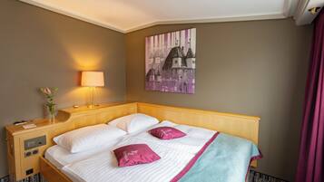 Habitación de hotel con una cama de madera, sábanas blancas, un plaid color turquesa y un cuadro de un paisaje urbano en la pared.