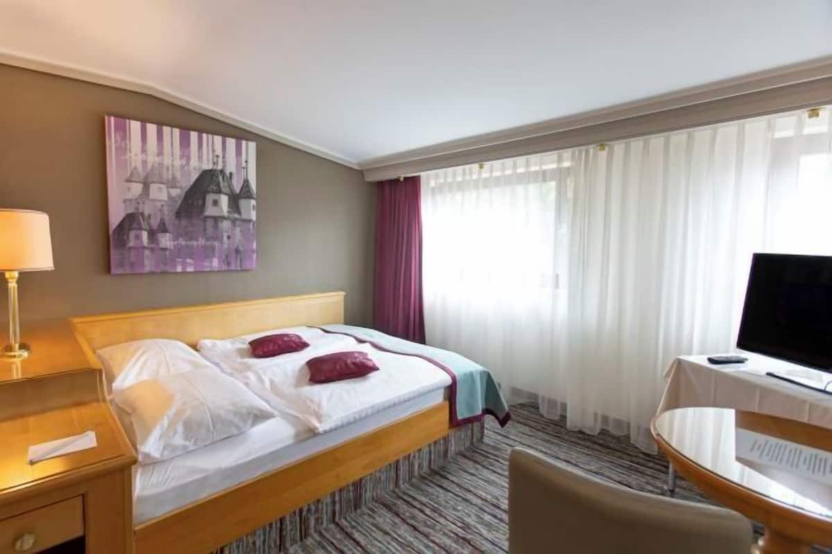 Ein Hotelzimmer mit Bett, Schreibtisch mit Computer, Fernseher und einem Bild an der Wand.