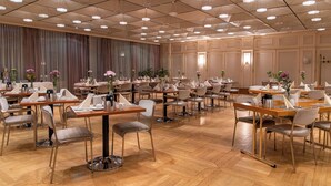A spacious dining area with multiple tables and chairs, a high ceiling with recessed lighting, and a large curtain backdrop.