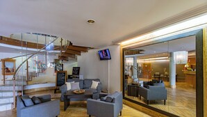 A modern lobby with a staircase, a seating area with sofas, a television, and a large mirror reflecting the interior.