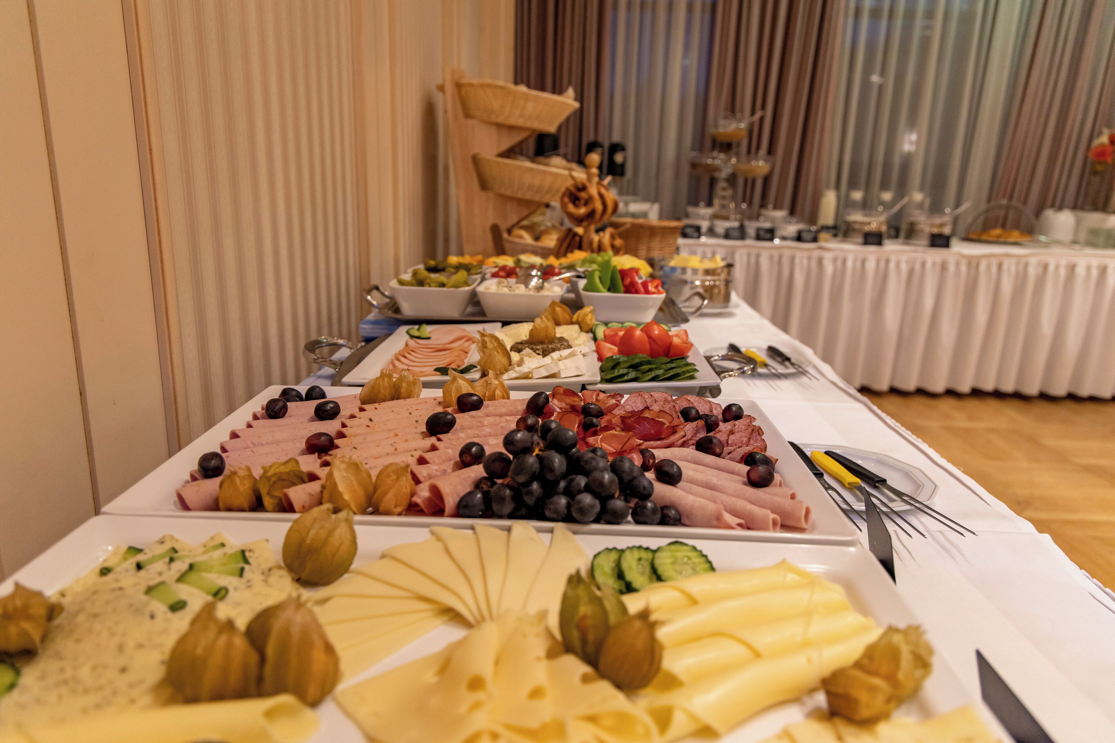 A buffet table with various cheeses, meats, and vegetables.