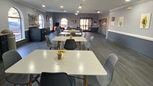 A dining area with tables and chairs, a kitchen in the background, and artwork on the walls. - Days Inn & Suites by Wyndham Winnie (Winnie)