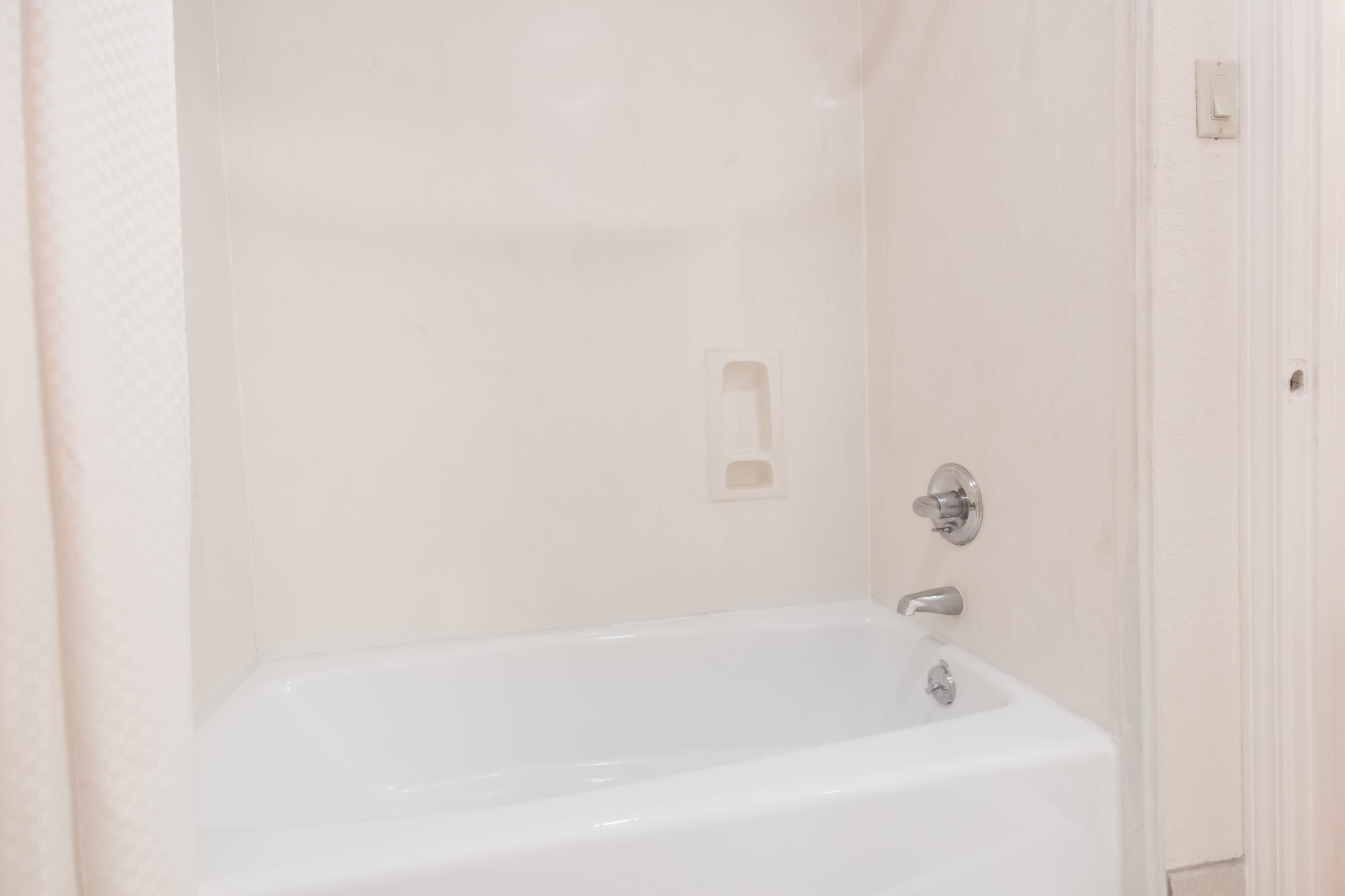 A white bathtub with a faucet and a control panel, a white door with a handle, and a light switch on the wall.