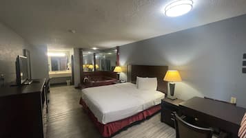 A hotel room with a bed, a desk, a chair, a mirror, and a lamp.