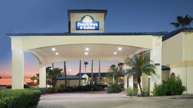 A Days Inn & Suites with a large entrance canopy, palm trees, and a parking lot. - Days Inn & Suites by Wyndham Winnie (Winnie)